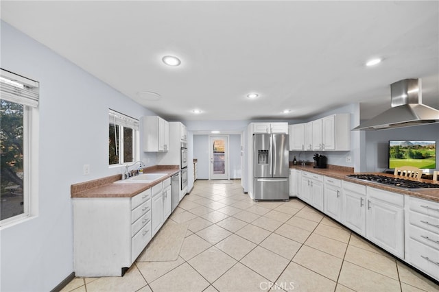 kitchen featuring white cabinets, wall chimney range hood, sink, appliances with stainless steel finishes, and light tile patterned flooring