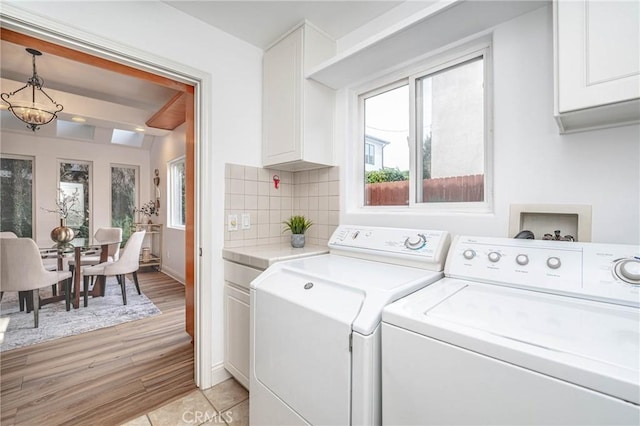 clothes washing area featuring cabinets, light wood-type flooring, and washing machine and clothes dryer