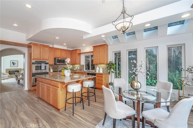 kitchen featuring light stone countertops, appliances with stainless steel finishes, tasteful backsplash, a center island with sink, and light hardwood / wood-style floors