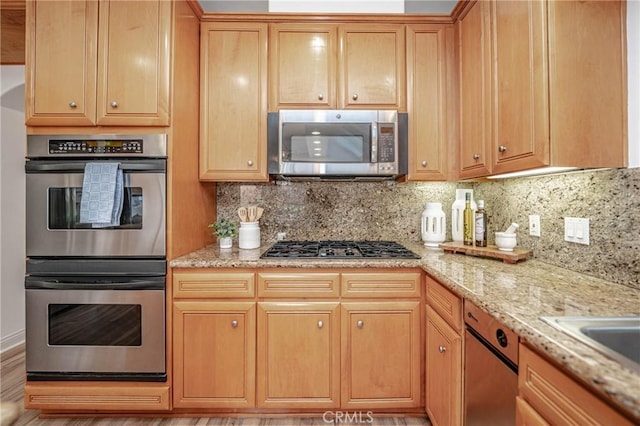 kitchen with decorative backsplash, light stone countertops, light wood-type flooring, and appliances with stainless steel finishes