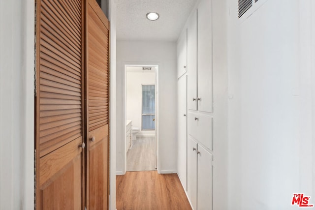 hallway with a textured ceiling and light hardwood / wood-style floors