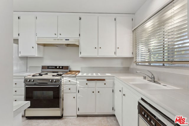 kitchen featuring sink, dishwasher, light tile patterned floors, white cabinets, and range