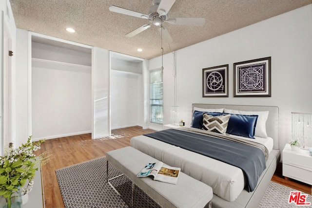 bedroom featuring multiple closets, ceiling fan, a textured ceiling, and hardwood / wood-style flooring