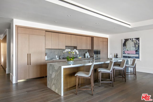 kitchen with decorative backsplash, a kitchen island with sink, sink, and dark hardwood / wood-style flooring