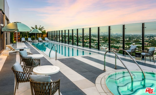 pool at dusk featuring an in ground hot tub and a patio area