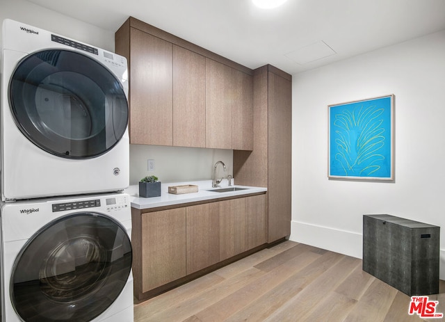 laundry area with stacked washer / dryer, sink, light hardwood / wood-style floors, and cabinets