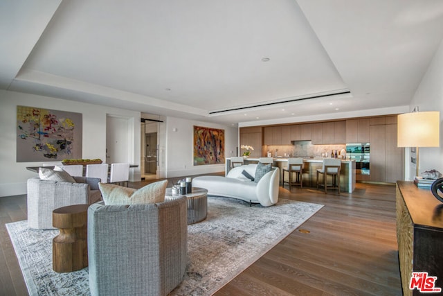 living room with a tray ceiling and dark wood-type flooring