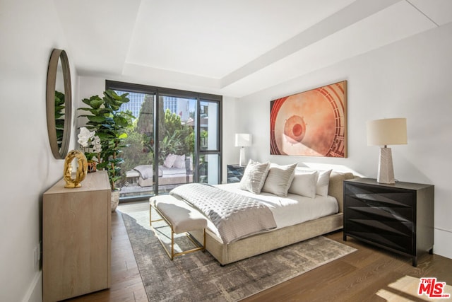 bedroom featuring access to outside, a tray ceiling, and dark wood-type flooring