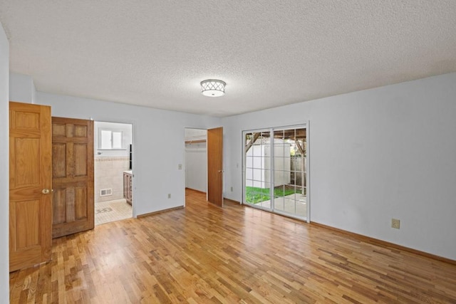 unfurnished bedroom featuring ensuite bath, access to outside, light hardwood / wood-style floors, and a textured ceiling