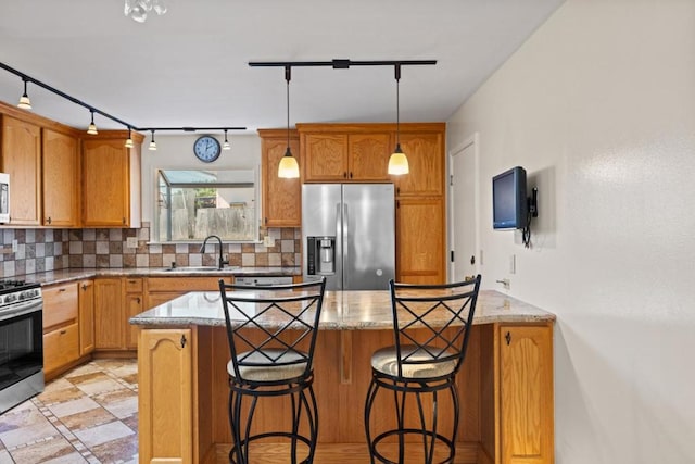 kitchen with sink, appliances with stainless steel finishes, hanging light fixtures, light stone counters, and decorative backsplash