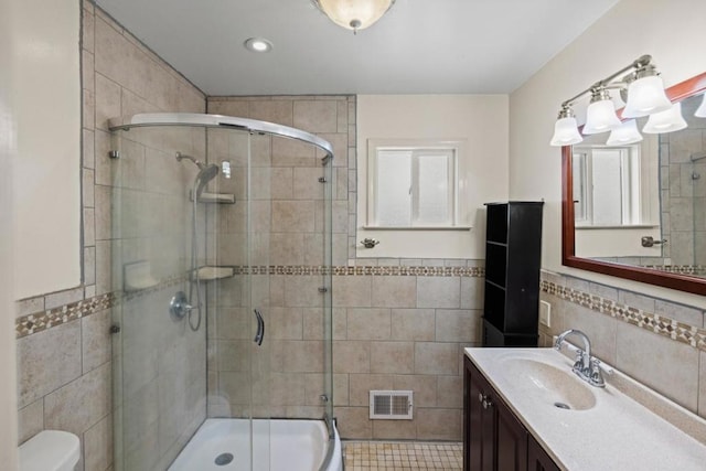 bathroom with vanity, toilet, a shower with shower door, and tile walls