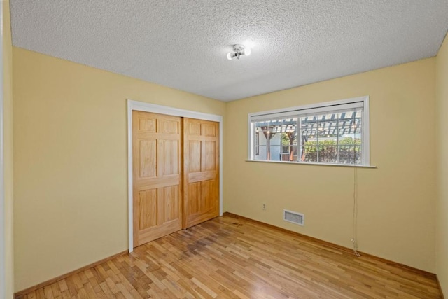 unfurnished bedroom featuring light hardwood / wood-style floors, a closet, and a textured ceiling