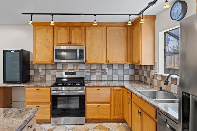 kitchen featuring sink, light stone counters, tasteful backsplash, track lighting, and stainless steel appliances