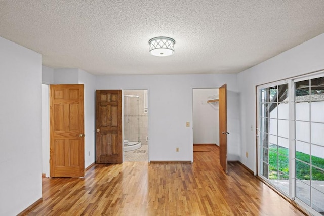 unfurnished bedroom with ensuite bath, access to exterior, light hardwood / wood-style floors, and a textured ceiling