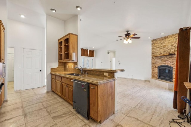 kitchen featuring dishwasher, sink, ceiling fan, dark stone countertops, and a fireplace