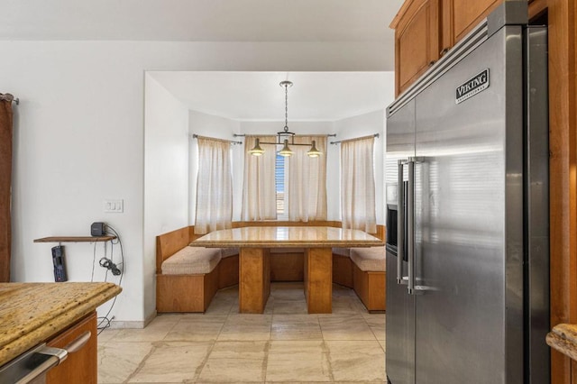 kitchen featuring hanging light fixtures, light stone counters, stainless steel built in fridge, and breakfast area