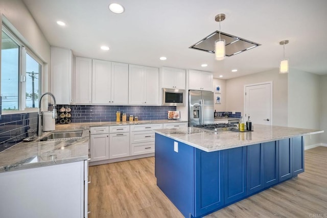 kitchen with light wood-type flooring, pendant lighting, sink, stainless steel appliances, and white cabinetry