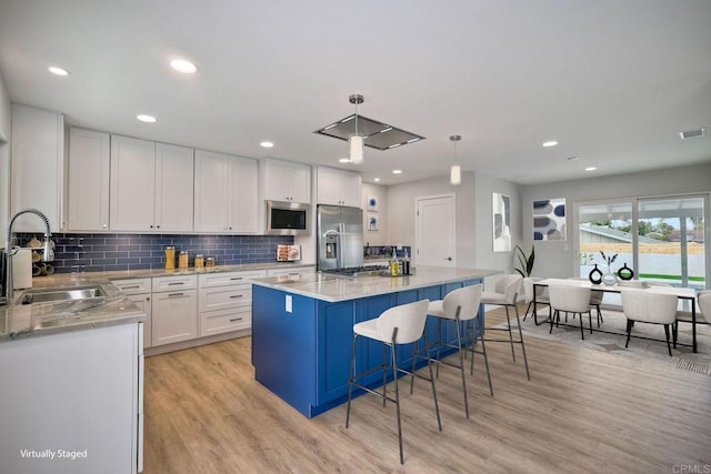 kitchen featuring a center island, stainless steel appliances, white cabinets, sink, and decorative light fixtures