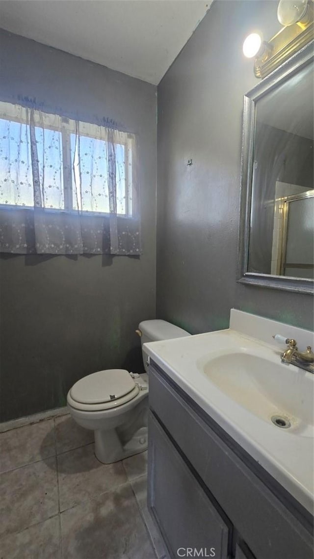 bathroom with an enclosed shower, vanity, toilet, and tile patterned flooring