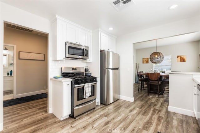 kitchen featuring backsplash, pendant lighting, light wood-type flooring, appliances with stainless steel finishes, and white cabinets