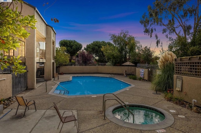 pool at dusk featuring a hot tub and a patio area