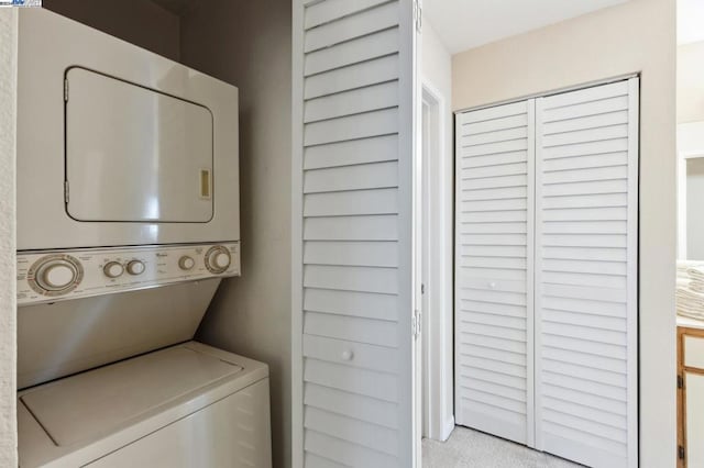 laundry area featuring stacked washer and dryer and light carpet