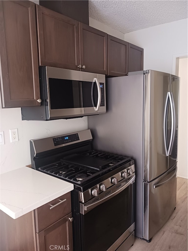 kitchen with dark brown cabinetry, a textured ceiling, stainless steel appliances, and light hardwood / wood-style floors