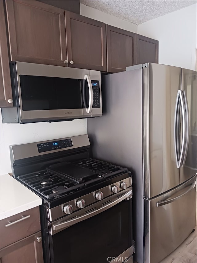 kitchen featuring dark brown cabinetry, a textured ceiling, and stainless steel appliances