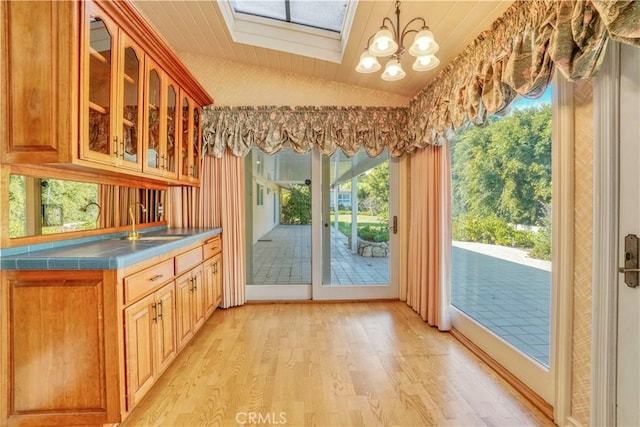 interior space featuring vaulted ceiling with skylight, light hardwood / wood-style flooring, plenty of natural light, and sink