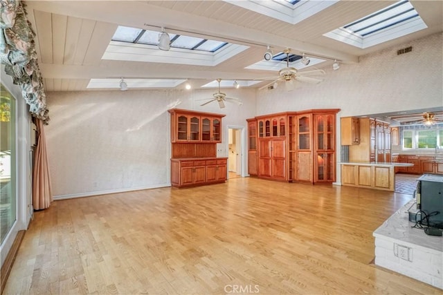 unfurnished living room with ceiling fan, beamed ceiling, high vaulted ceiling, and light wood-type flooring