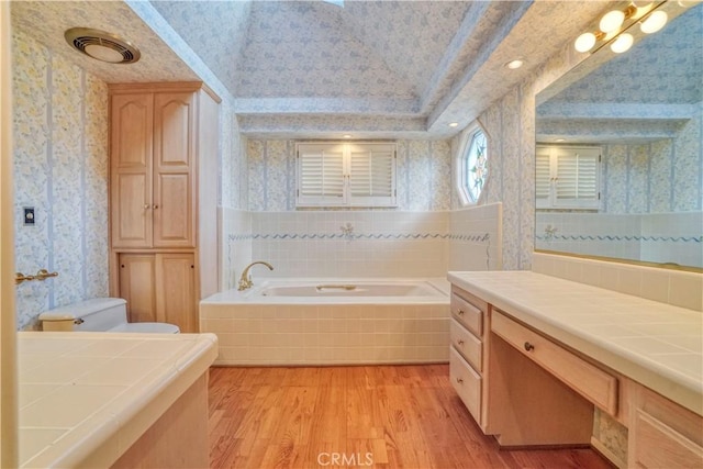 bathroom featuring vanity, toilet, wood-type flooring, and tiled tub