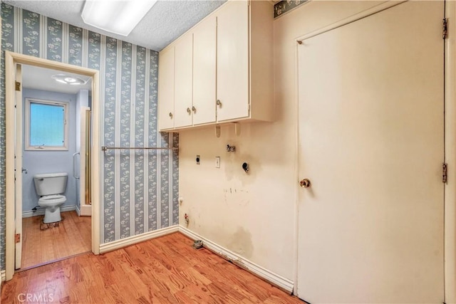 clothes washing area with cabinets, hookup for an electric dryer, light hardwood / wood-style flooring, hookup for a washing machine, and a textured ceiling