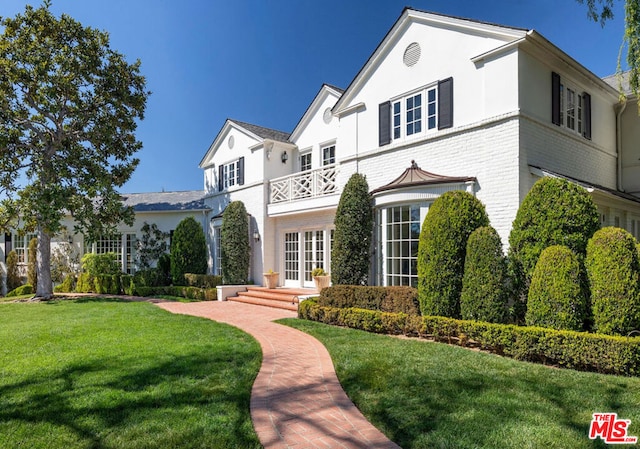 view of front of home with french doors, a balcony, and a front lawn