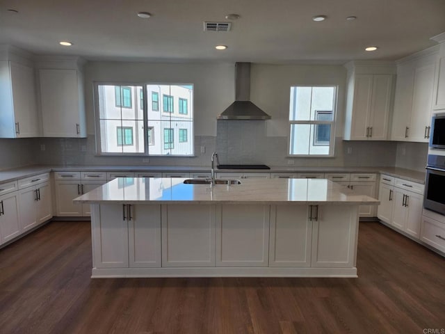 kitchen featuring dark wood-style floors, wall chimney exhaust hood, a sink, and white cabinets