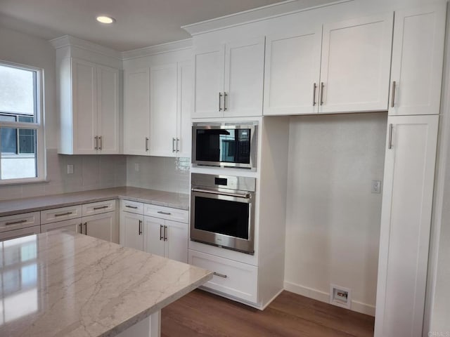 kitchen with light stone counters, dark wood finished floors, stainless steel appliances, backsplash, and white cabinets