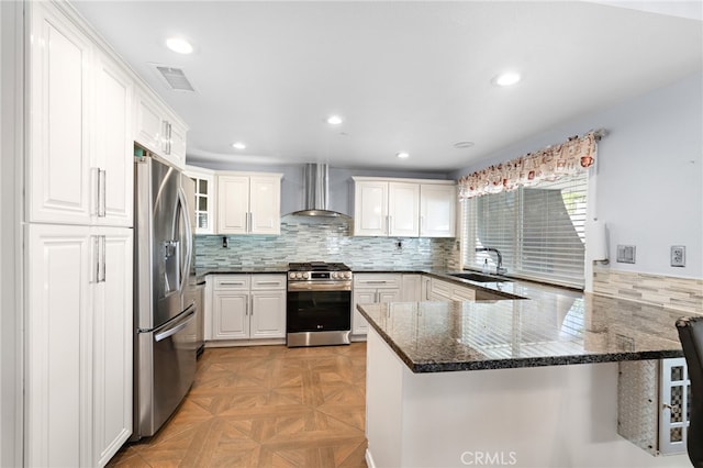 kitchen with white cabinets, kitchen peninsula, wall chimney range hood, stainless steel appliances, and light parquet floors