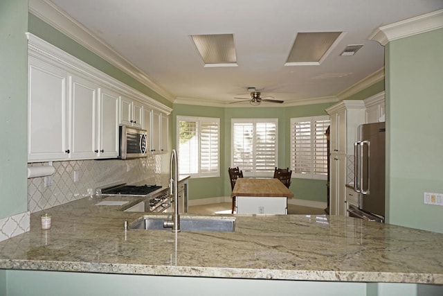 kitchen with ornamental molding, appliances with stainless steel finishes, kitchen peninsula, and white cabinetry