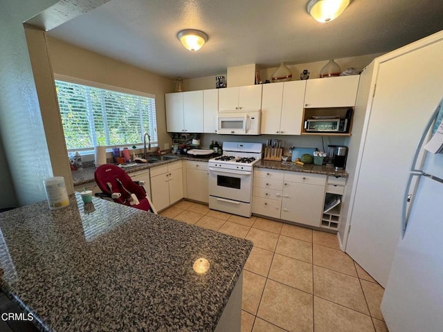 kitchen featuring dark stone counters, sink, light tile patterned flooring, white cabinets, and white appliances