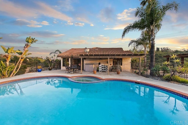 pool at dusk featuring an in ground hot tub and a patio