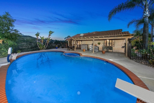 pool at dusk with a diving board and a patio area