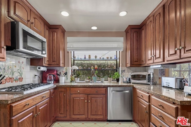 kitchen with backsplash, sink, dark stone counters, and stainless steel appliances