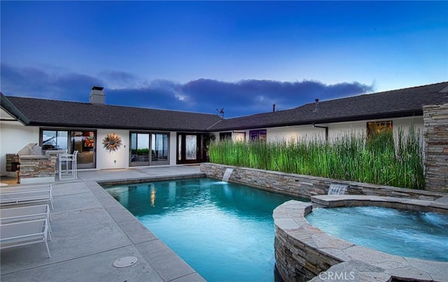 pool at dusk with an in ground hot tub, a patio area, pool water feature, and area for grilling