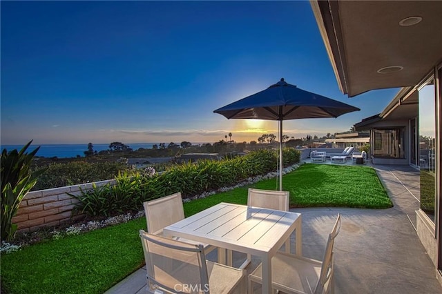 patio terrace at dusk featuring a water view and a yard