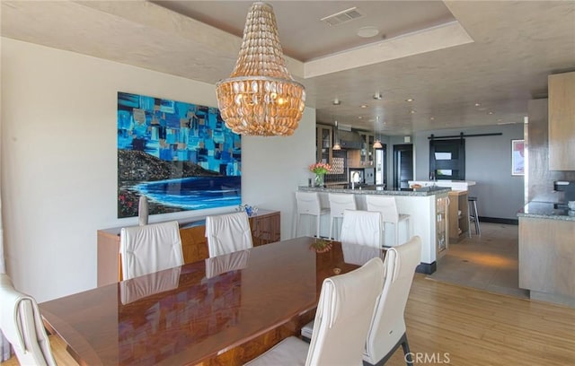 dining space featuring an inviting chandelier, a barn door, and light hardwood / wood-style flooring