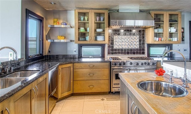 kitchen featuring wall chimney exhaust hood, sink, dark stone countertops, and stainless steel appliances