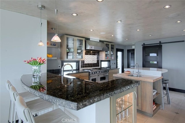 kitchen with a barn door, kitchen peninsula, range with two ovens, a kitchen breakfast bar, and pendant lighting