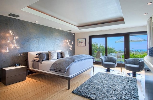 bedroom with light wood-type flooring and a tray ceiling