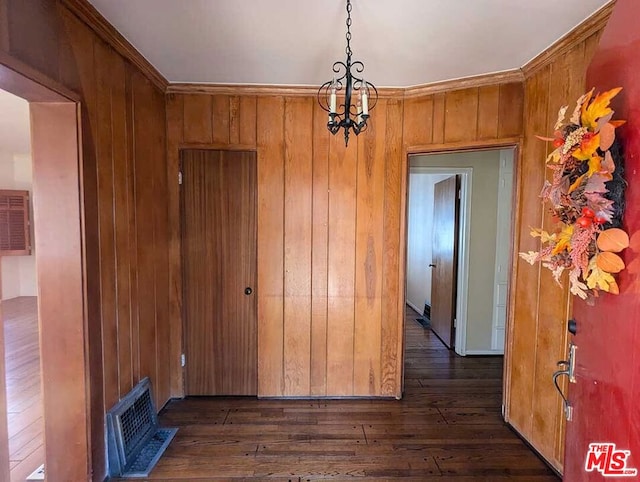 unfurnished dining area with dark hardwood / wood-style floors, wood walls, ornamental molding, and an inviting chandelier