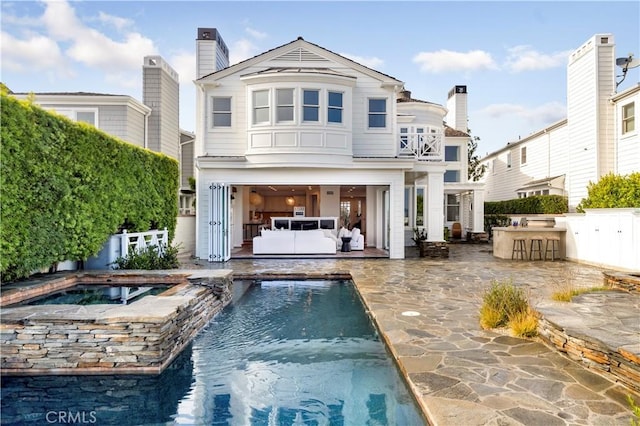 back of property featuring a swimming pool with hot tub, a balcony, and a patio area