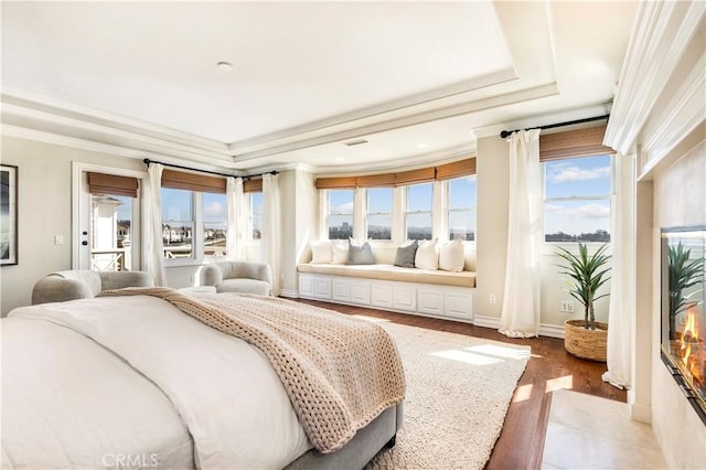 bedroom with a tray ceiling, multiple windows, crown molding, and wood-type flooring